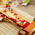 TsukiAshi Baumwoll Y-Geschirr aus einem roten Stoff mit ummantelten Rückensteg, Brussteg und Schulterpolster. Die Metalle sind aus Acetal und Messing in nahaufnahme.