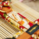 TsukiAshi Baumwoll Y-Geschirr aus einem roten Stoff mit ummantelten Rückensteg, Brussteg und Schulterpolster. Die Metalle sind aus Acetal und Messing in nahaufnahme.